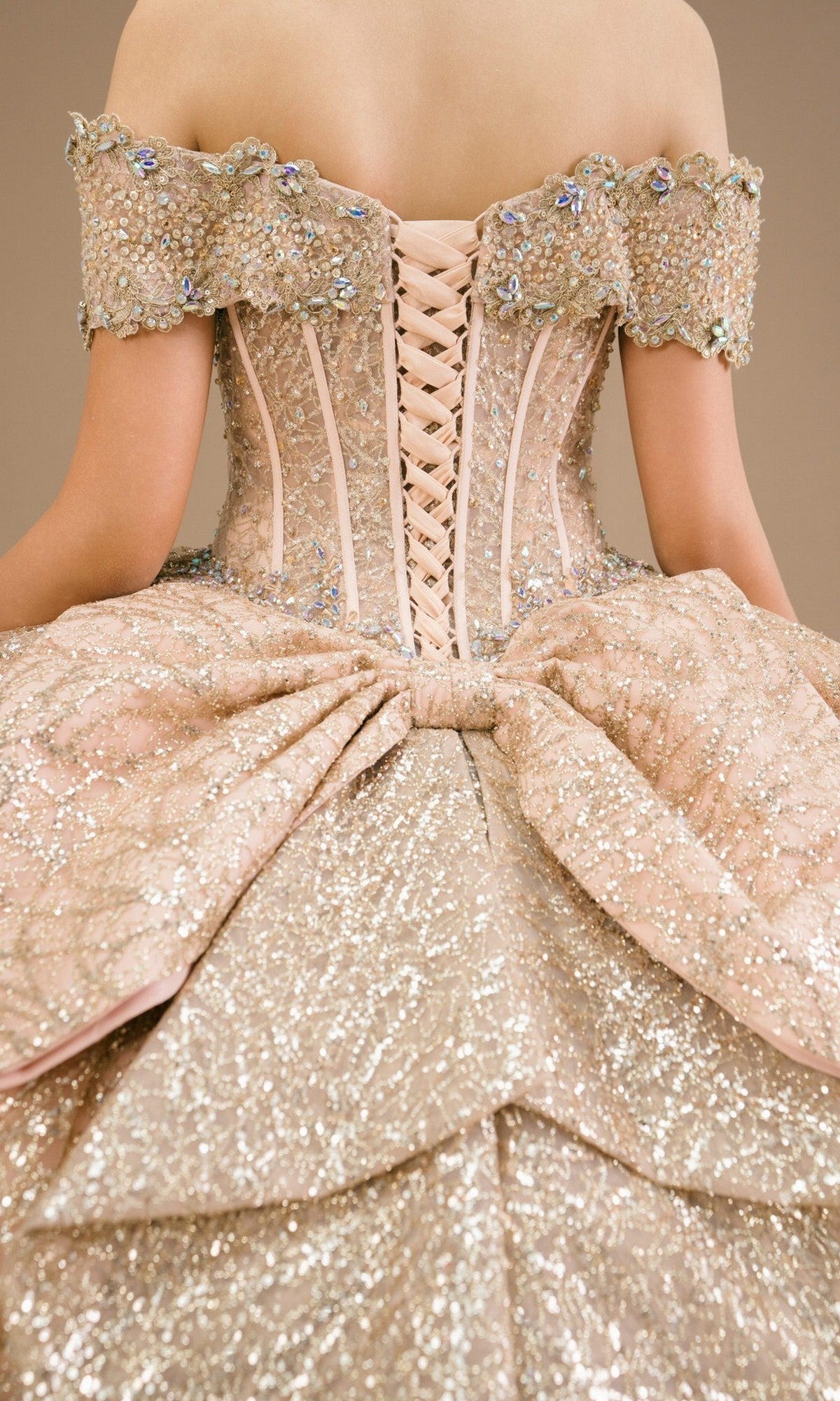 Close-up of a person wearing the Quinceanera Dress 8600JQ By Cinderella Couture, a sparkling gold ball gown featuring an off-the-shoulder neckline, large bow accent, corset-style lace-up back, and exquisite beading and sequin embellishments.